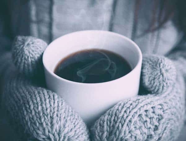 Warm mittens holding a hot coffee mug.